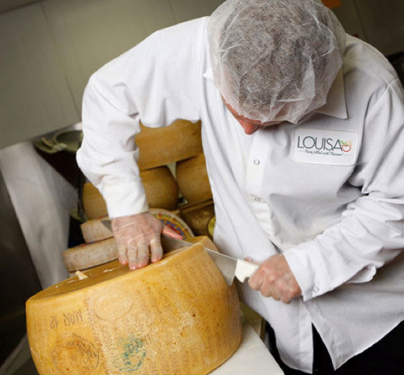 a Louisa chef cutting into a wheel of Parmesan cheese